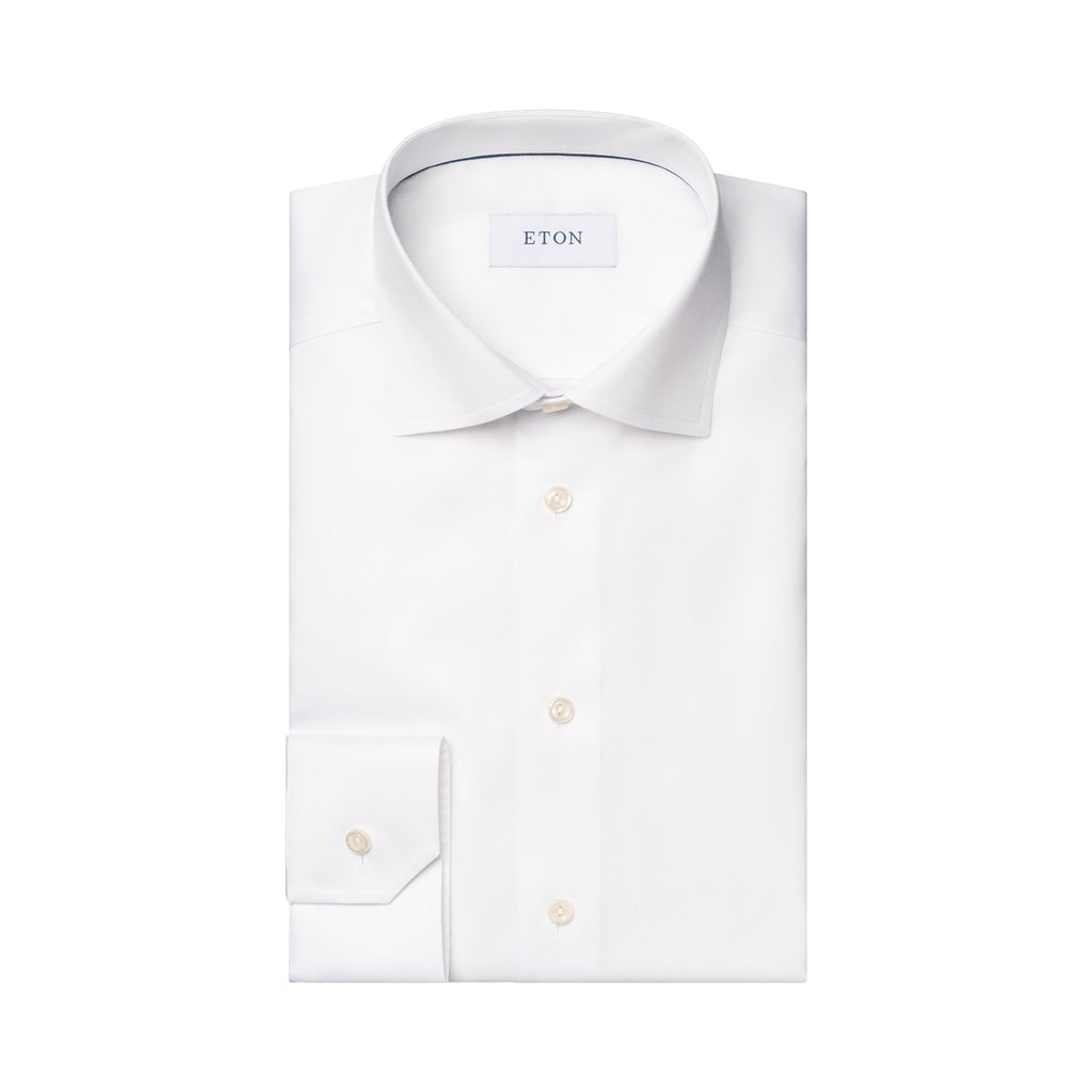 A folded white long-sleeve dress shirt with a pointed collar, button-down front, and a single-button cuff, shown on a plain white background. The neck label reads ETON. Eton Shirt. Sakks Menswear Southampton.