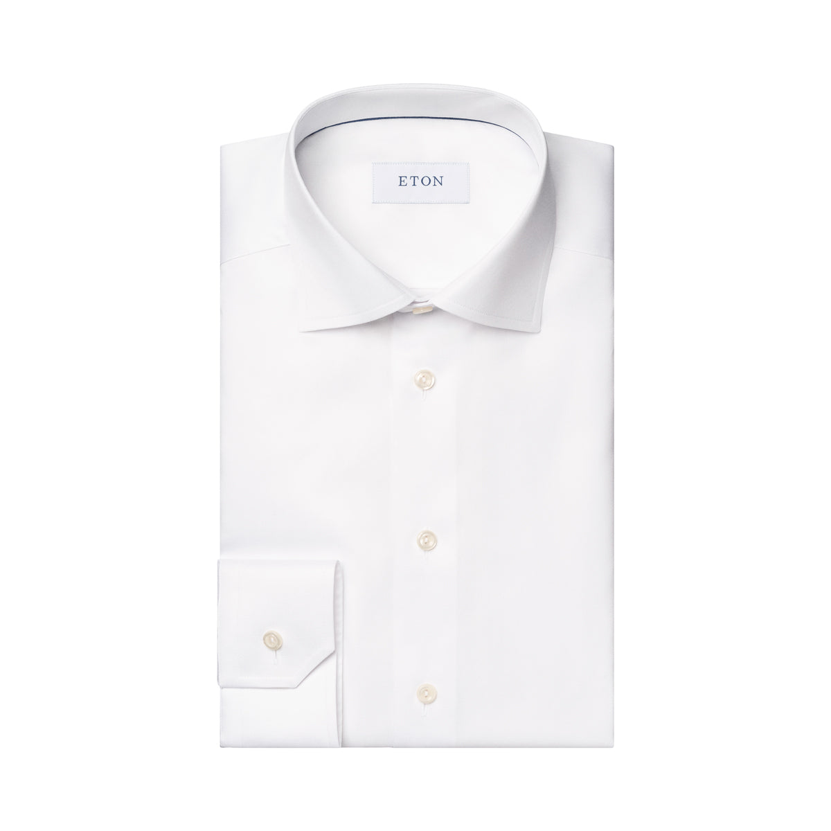 A folded white long-sleeve dress shirt with a pointed collar, button-down front, and a single-button cuff, shown on a plain white background. The neck label reads ETON. Eton Shirt. Sakks Menswear Southampton.