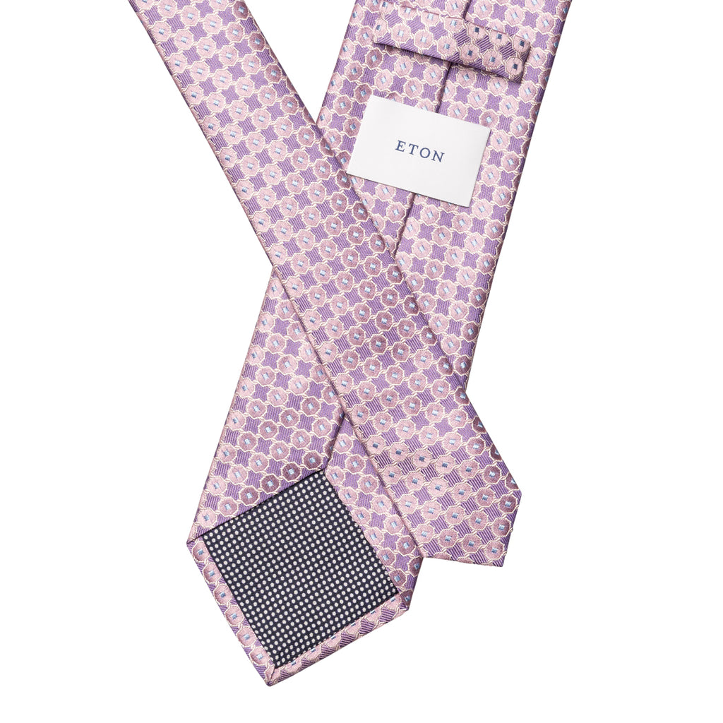 A lavender and white patterned silk tie with a white brand tag reading 'ETON' and a dark patterned neck blade, shown on a plain white background. Eton Ties available at Sakks Menswear in Southampton.