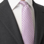 A close-up of a men's necktie with a lavender and beige geometric pattern, styled on a white dress shirt and dark gray suit jacket. Eton Ties available at Sakks Menswear in Southampton.