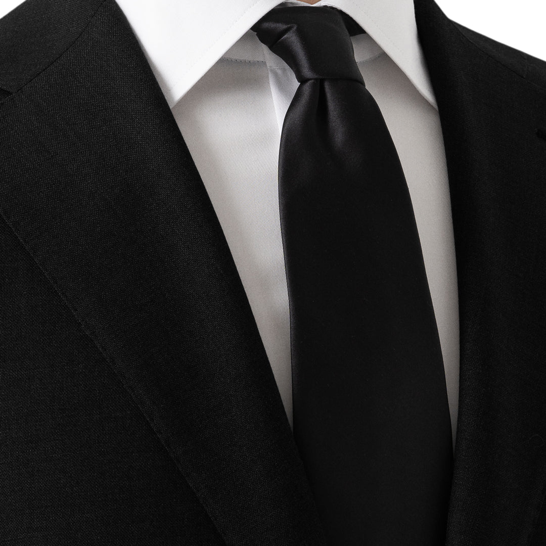 A classic black necktie neatly knotted and styled with a white dress shirt and a black suit jacket. Eton Ties available at Sakks Menswear in Southampton.