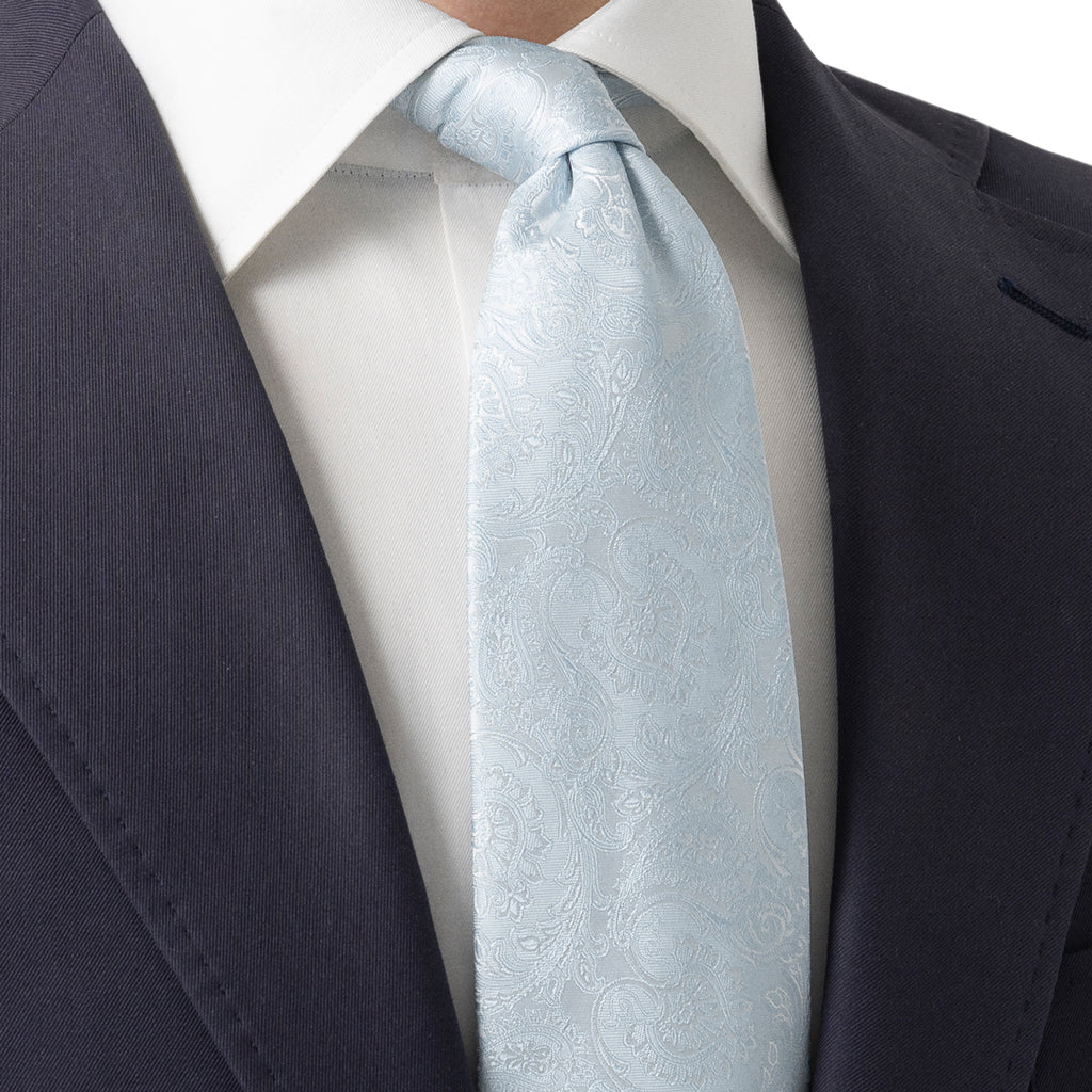 A light blue paisley patterned silk necktie, knotted and styled with a white dress shirt and a dark navy suit jacket. Eton Ties available at Sakks Menswear in Southampton.