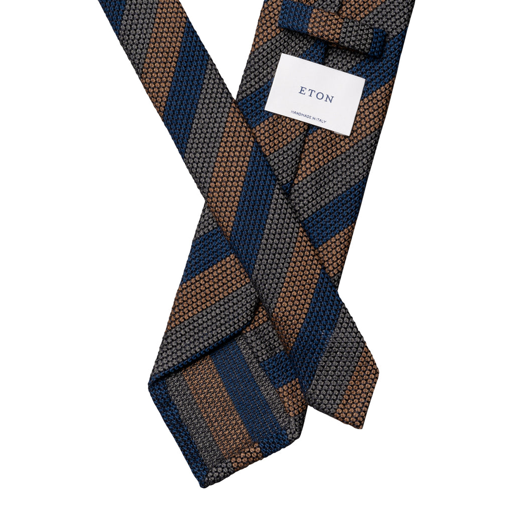 A folded Eton men's necktie with a textured geometric pattern of navy blue, brown, and gray diagonal stripes, featuring a white brand label. Eton Ties available at Sakks Menswear in Southampton.