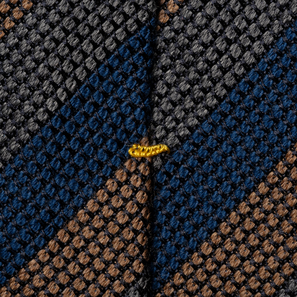Close-up of a textured woven fabric with a geometric pattern in dark gray, navy blue, and brown, featuring a small yellow embroidered accent near the center. Eton Ties available at Sakks Menswear in Southampton.