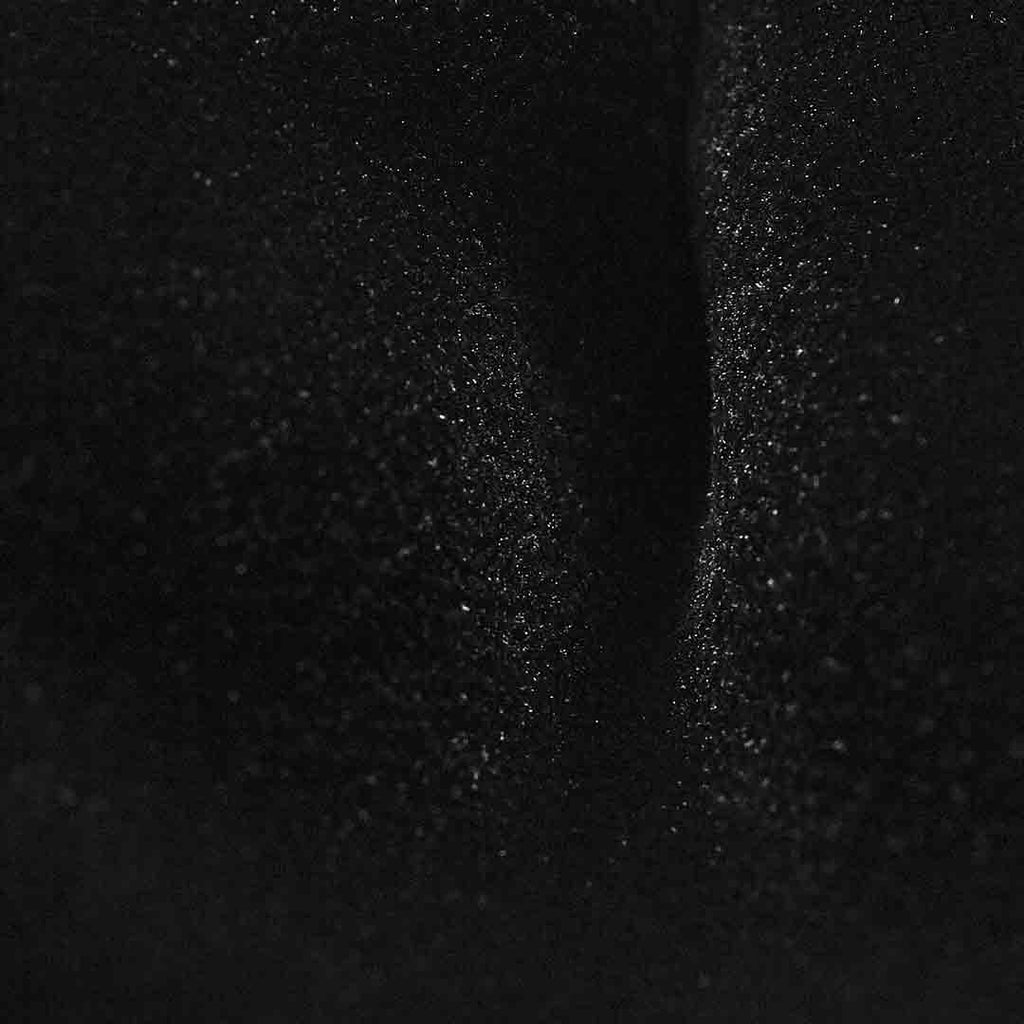 A close-up of a black textured material with fine glitter or speckled shimmer, showing soft folds and reflective highlights.  Bow Ties available at Sakks Menswear in Southampton.