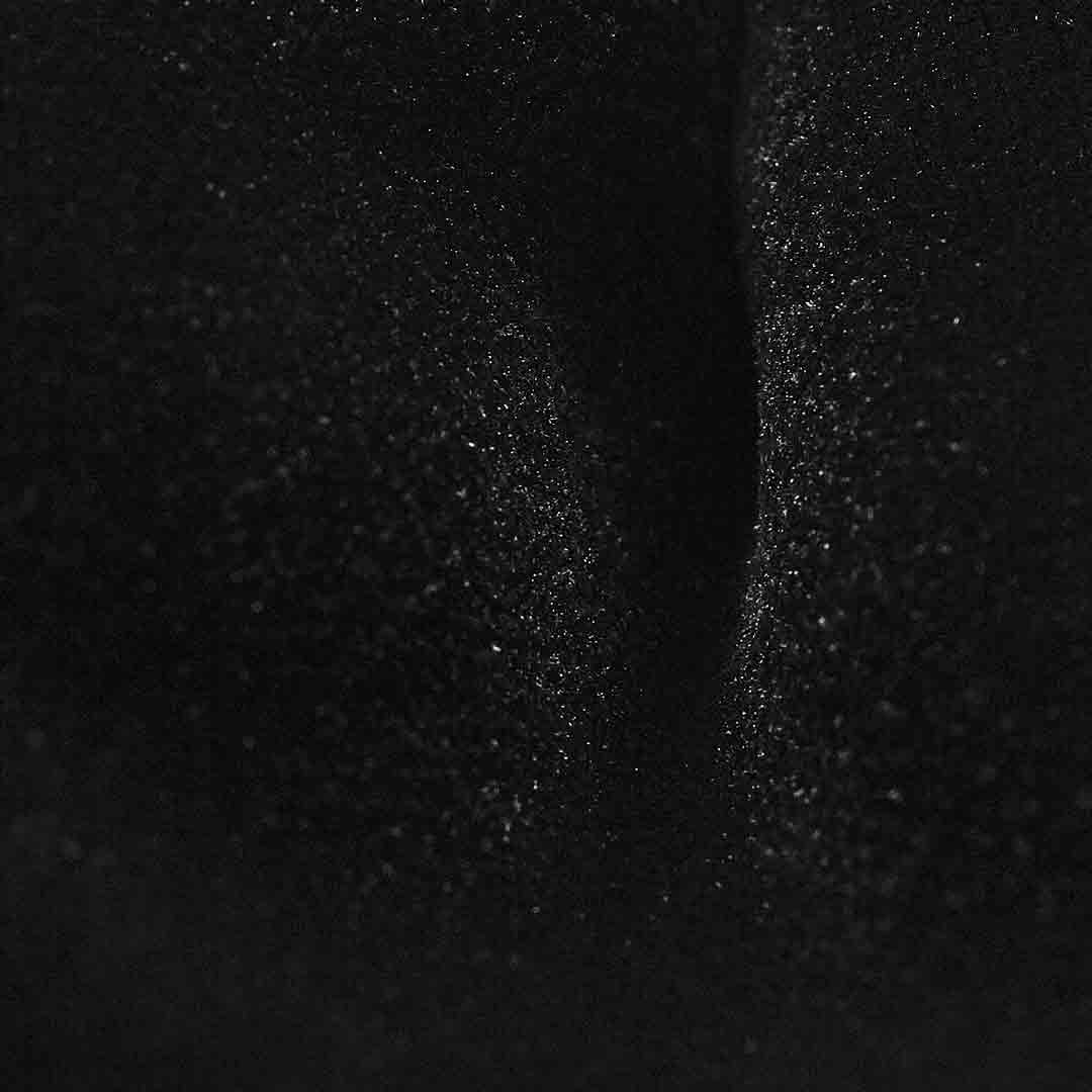 A close-up of a black textured material with fine glitter or speckled shimmer, showing soft folds and reflective highlights.  Bow Ties available at Sakks Menswear in Southampton.