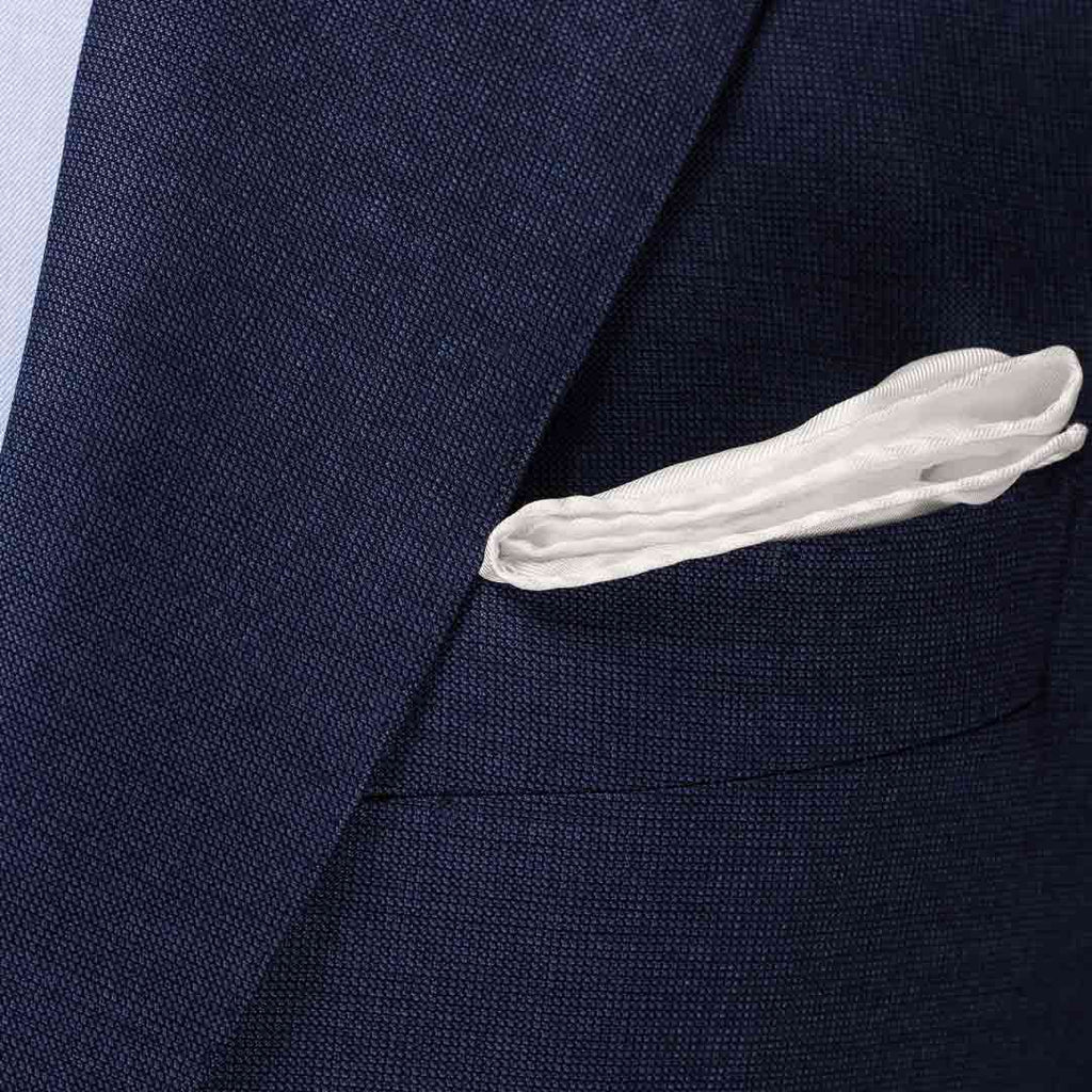 Close-up of a navy blue textured suit jacket with a white pocket square tucked into the breast pocket. Eton Pocket Square available at Sakks Menswear in Southampton.