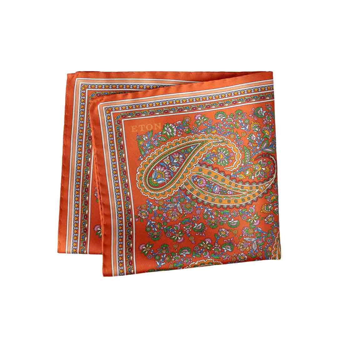 An orange silk scarf with a detailed paisley pattern in green, gold, and blue, featuring the brand name 'ETON' printed in gold near the top left corner. Eton Pocket Square available at Sakks Menswear in Southampton.
