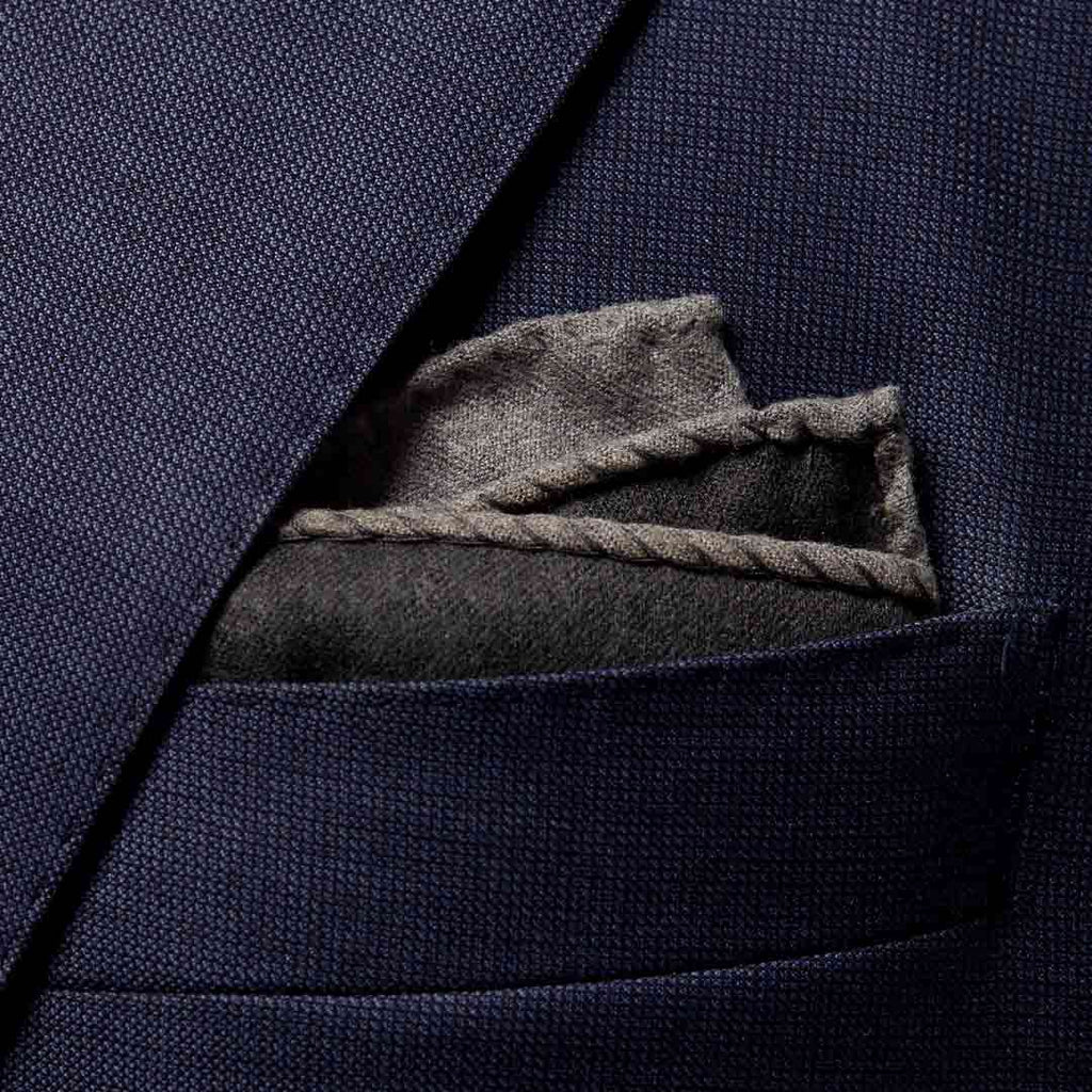 A close-up of a navy blue textured suit jacket pocket with a folded gray pocket square tucked inside. Eton Pocket Square available at Sakks Menswear in Southampton.