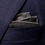 A close-up of a navy blue textured suit jacket pocket with a folded gray pocket square tucked inside. Eton Pocket Square available at Sakks Menswear in Southampton.