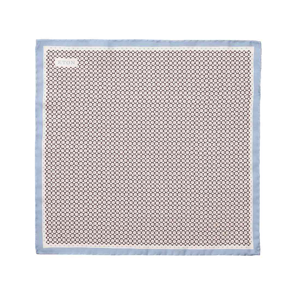A square silk scarf with a repeating geometric pattern in brown and beige, finished with a light blue border, shown flat against a white background. Eton Pocket Square available at Sakks Menswear in Southampton.
