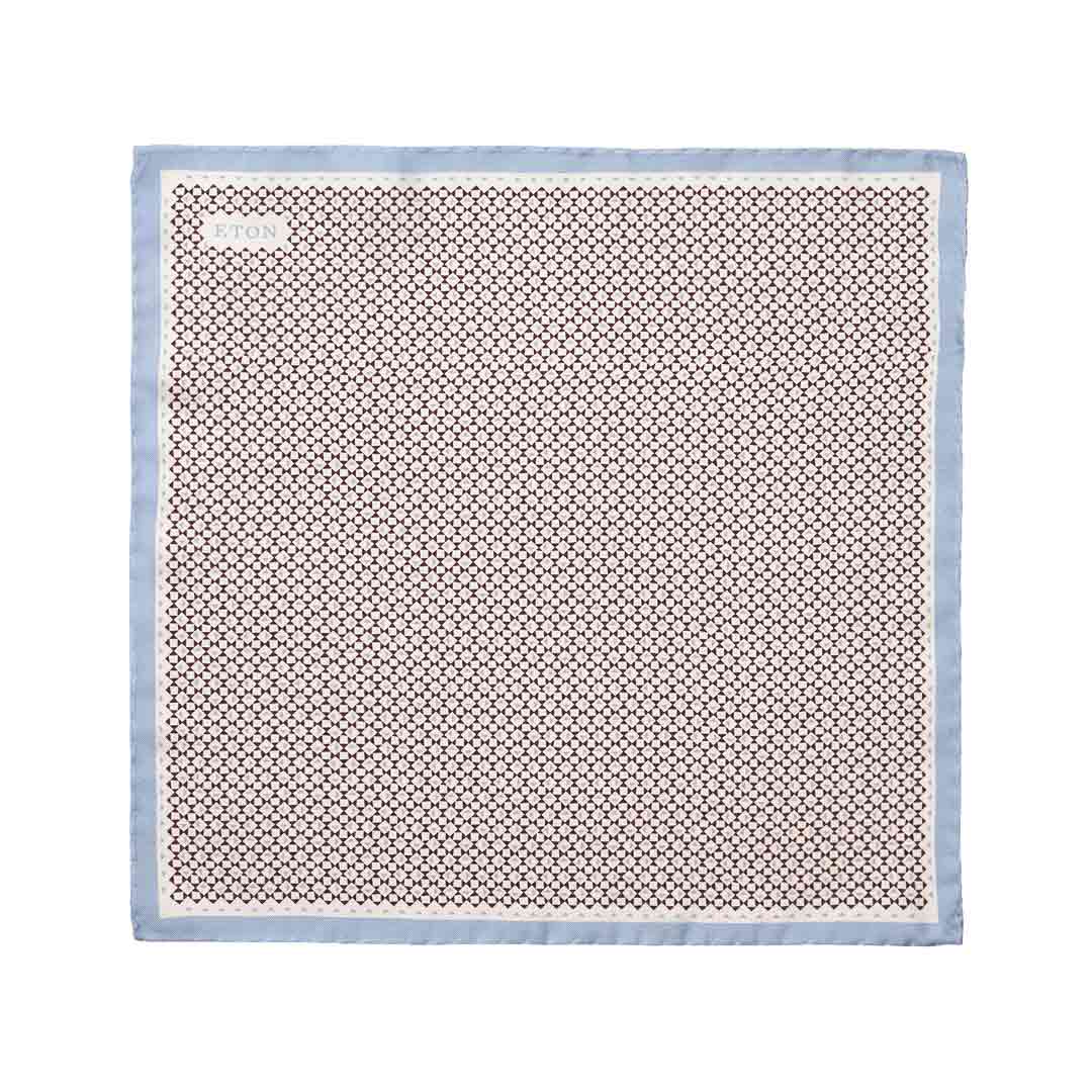A square silk scarf with a repeating geometric pattern in brown and beige, finished with a light blue border, shown flat against a white background. Eton Pocket Square available at Sakks Menswear in Southampton.