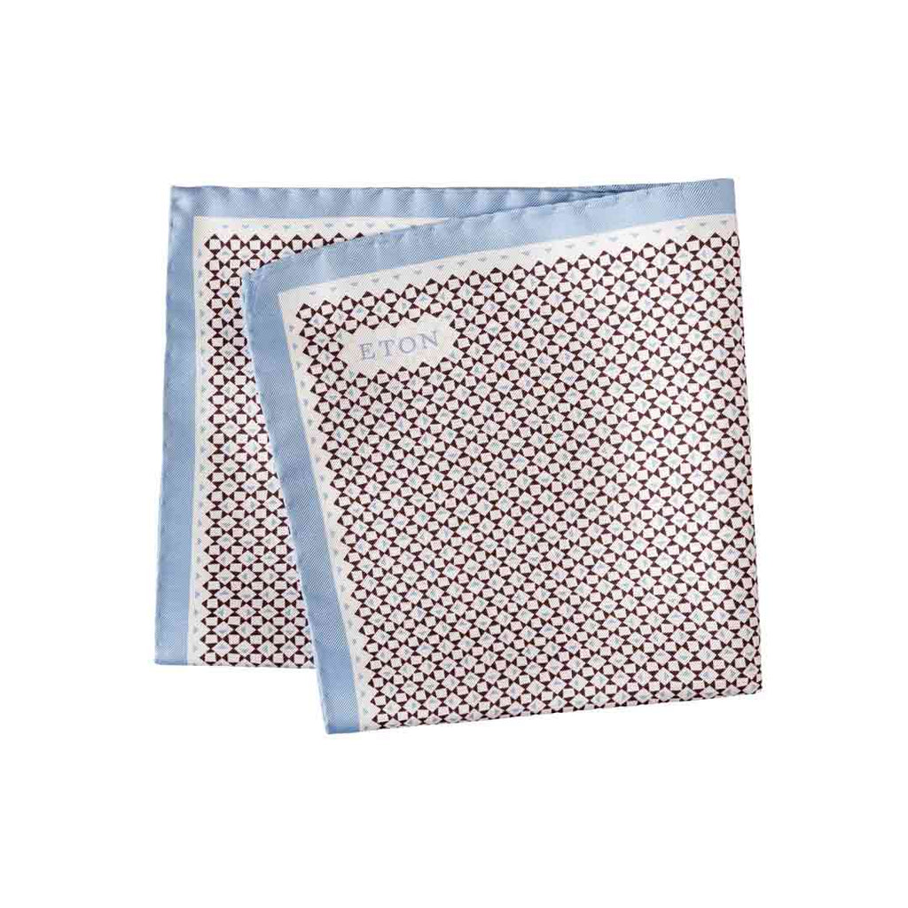 A folded square pocket square with a repeating geometric pattern in dark brown and white, finished with a light blue border. The brand name 'ETON' is printed on a small white label on one corner. Eton Pocket Square available at Sakks Menswear in Southampton.