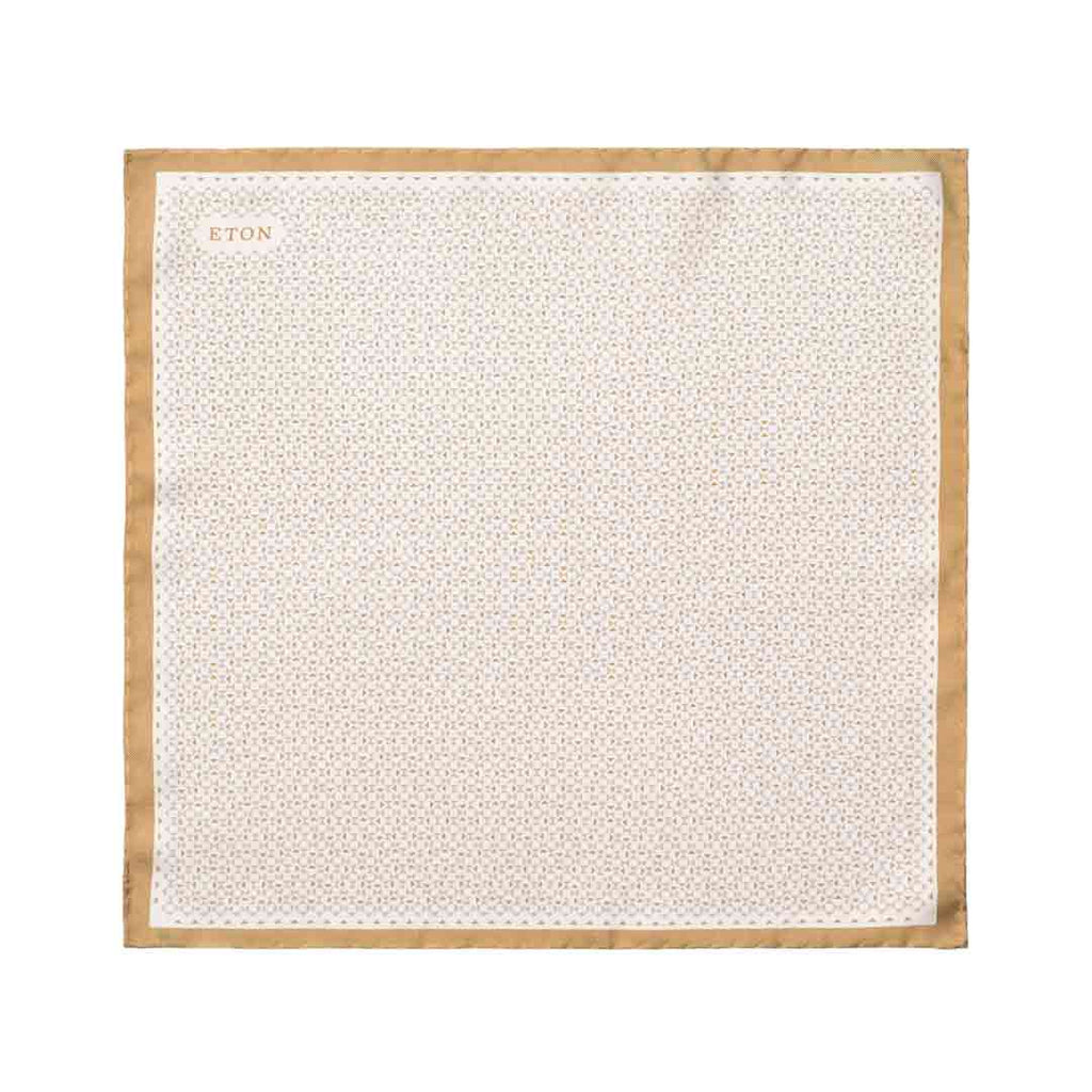 A square white pocket square with a repeating geometric pattern and a tan border, featuring the brand name 'ETON' printed in the top left corner. Eton Pocket Square available at Sakks Menswear in Southampton.