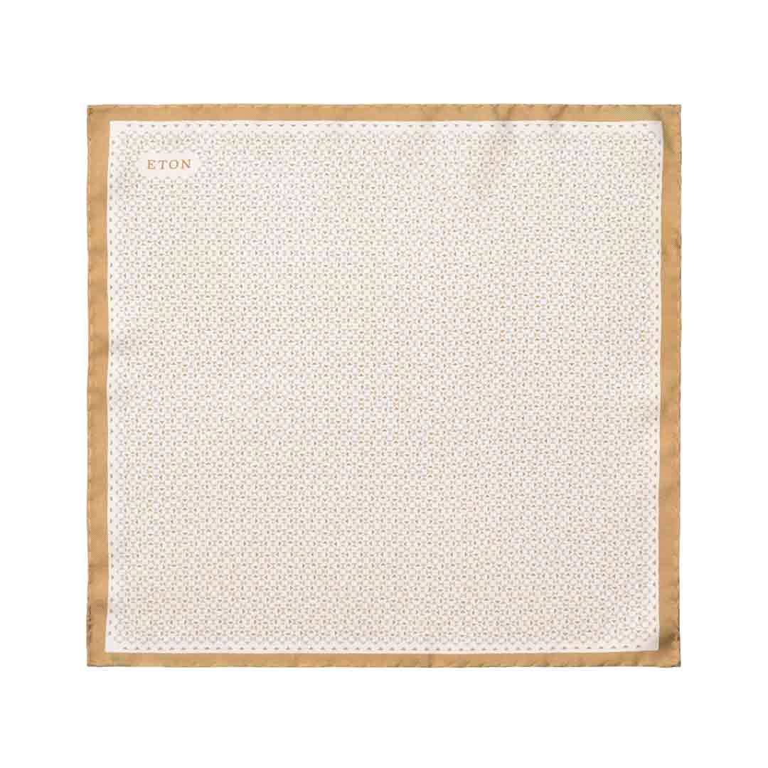 A square white pocket square with a repeating geometric pattern and a tan border, featuring the brand name 'ETON' printed in the top left corner. Eton Pocket Square available at Sakks Menswear in Southampton.