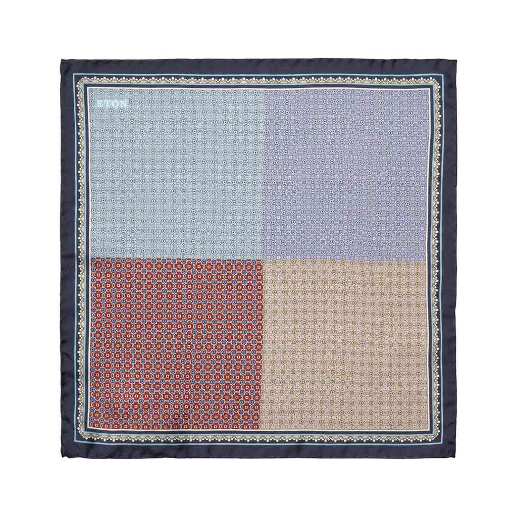 A square pocket square with a four-quadrant patterned design in light blue, lavender, rust red, and beige, framed by a dark navy border with a decorative geometric pattern. Eton Pocket Square available at Sakks Menswear in Southampton.