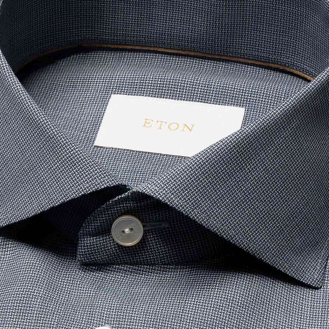 Close-up of a textured ETON dress shirt collar with a white neck label featuring gold lettering and a single button. Eton Shirt available at Sakks Menswear in Southampton.
