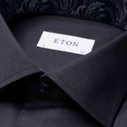 Close-up of a dark charcoal gray dress shirt collar with a white neck label reading ETON, showing part of a patterned inner collar lining. Eton Shirt available at Sakks Menswear in Southampton.