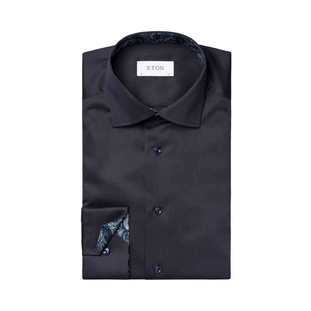 A folded black dress shirt with a patterned inner collar and cuff, featuring a white neck label that reads 'ETON', set against a plain white background. Eton Shirt available at Sakks Menswear in Southampton.