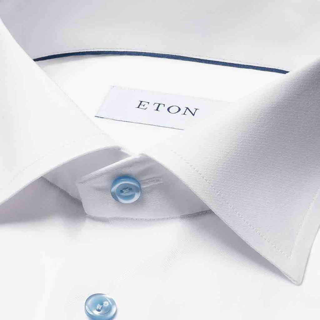 Close-up of a white dress shirt collar with a light blue button and a visible ETON neck label. Eton Shirt available at Sakks Menswear in Southampton.