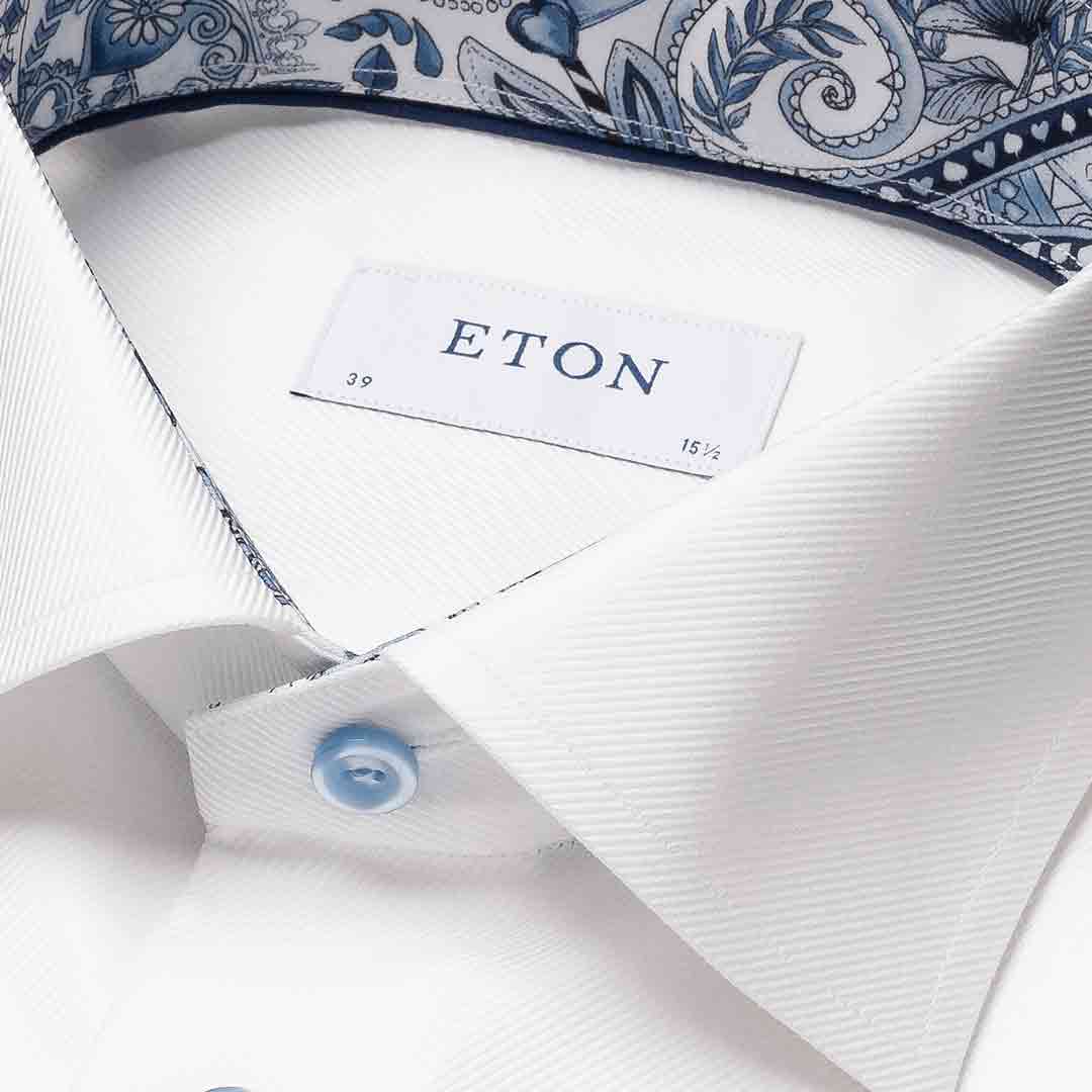 Close-up of a white ETON dress shirt collar with a light blue button and a blue paisley-patterned inner neck lining. Eton Shirt available at Sakks Menswear in Southampton.