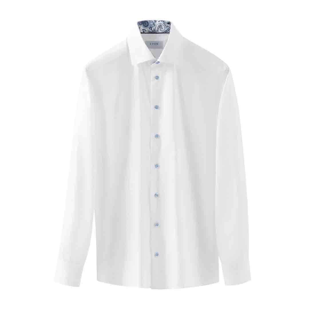 A white long-sleeve button-down dress shirt with a pointed collar and light blue buttons, displayed on a hanger with a patterned neck band against a plain white background. Eton Shirt available at Sakks Menswear in Southampton.