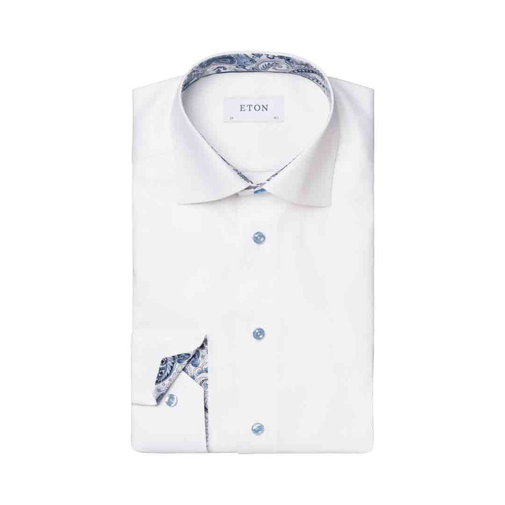 A folded white dress shirt with a blue paisley patterned inner collar and matching pocket square, featuring light blue buttons and the brand name ETON on the collar label. Eton Shirt available at Sakks Menswear in Southampton.