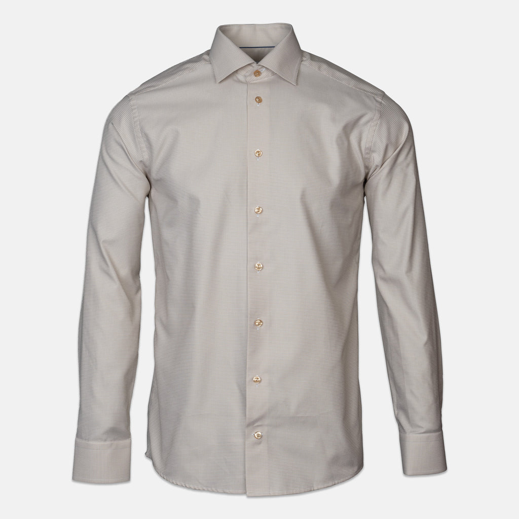 A light beige shirt with brown buttons in front of a light grey background. Eton shirts available at Sakks Menswear in Southampton.