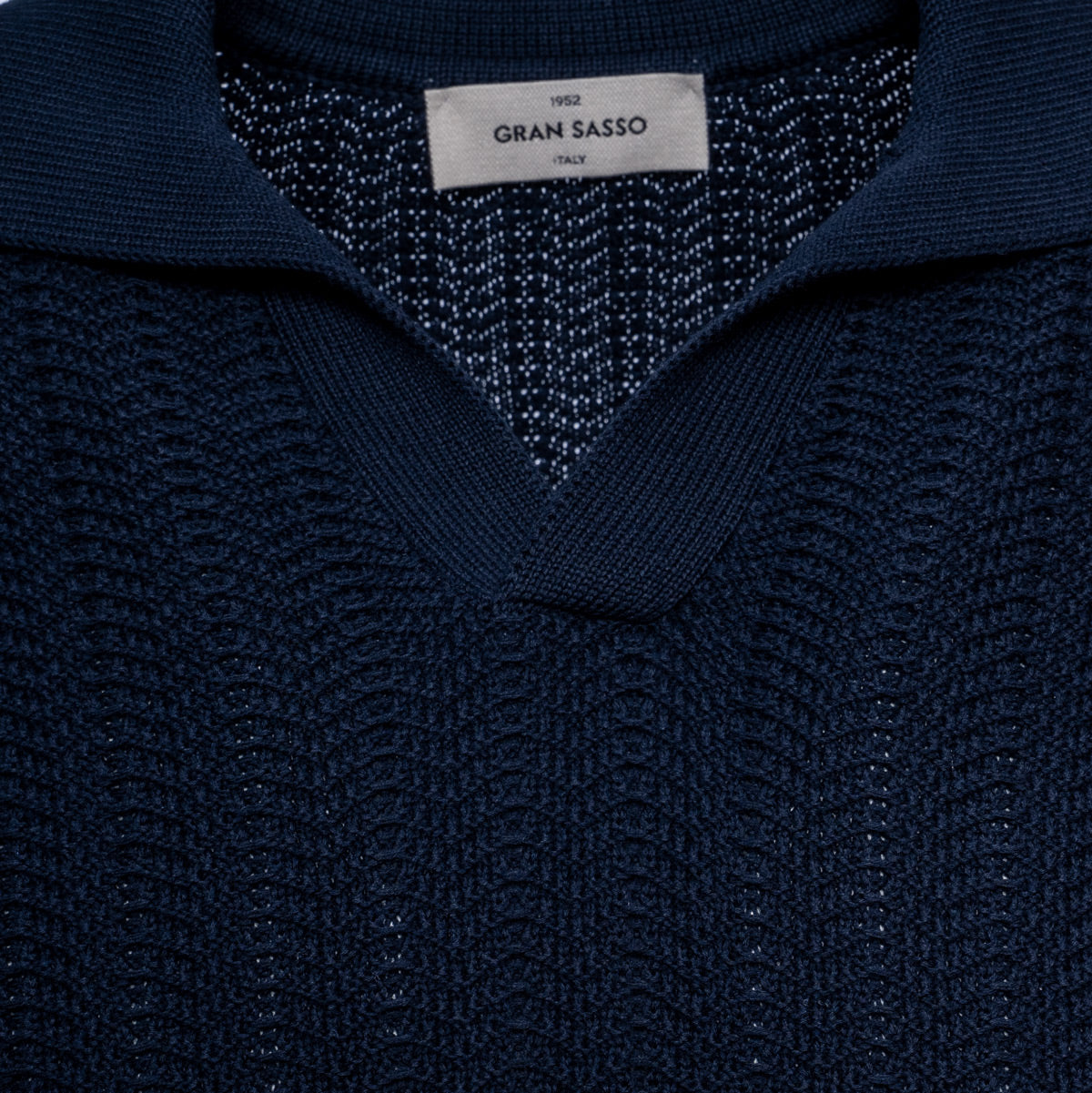 Close-up of a dark navy blue knit sweater with a textured pattern and a white brand label reading 'GRAN SASSO' at the collar. Gran Sasso Polo available at Sakks Menswear in Southampton.