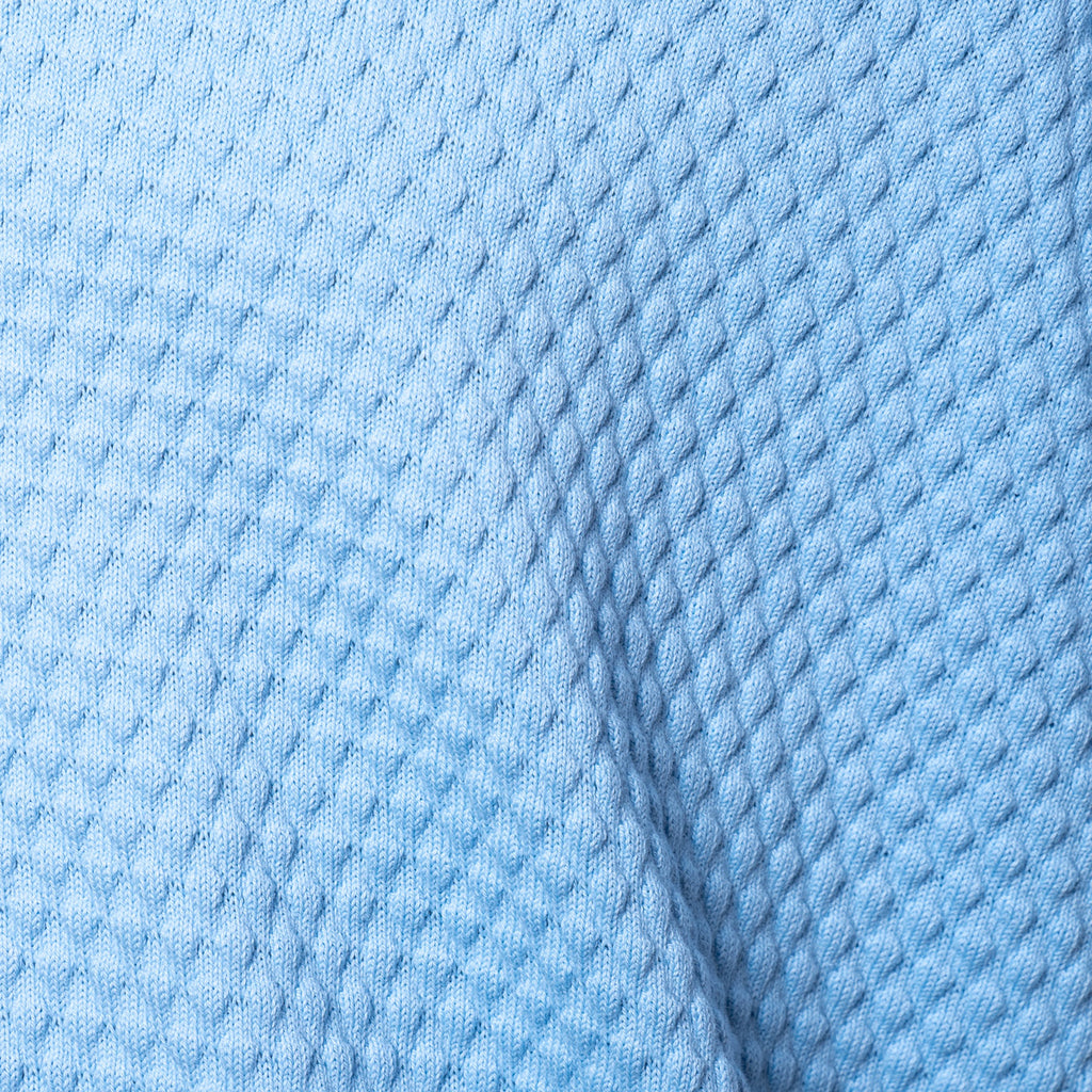 A close-up of light blue textured fabric with a waffle or diamond knit pattern and a soft fold. Gran Sasso Polo available at Sakks Menswear in Southampton.