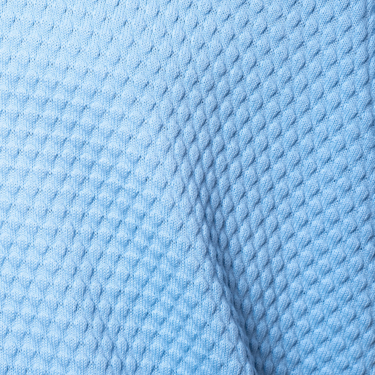 A close-up of light blue textured fabric with a waffle or diamond knit pattern and a soft fold. Gran Sasso Polo available at Sakks Menswear in Southampton.