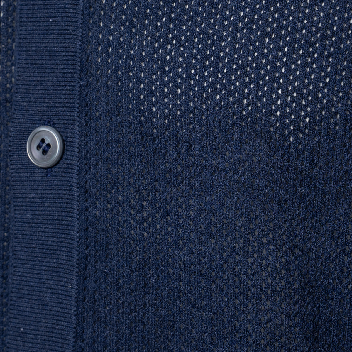 Close-up of a navy blue knit cardigan or sweater showing the ribbed button placket, a single silver button, and a textured dotted knit pattern. Gran Sasso Polo available at Sakks Menswear in Southampton.