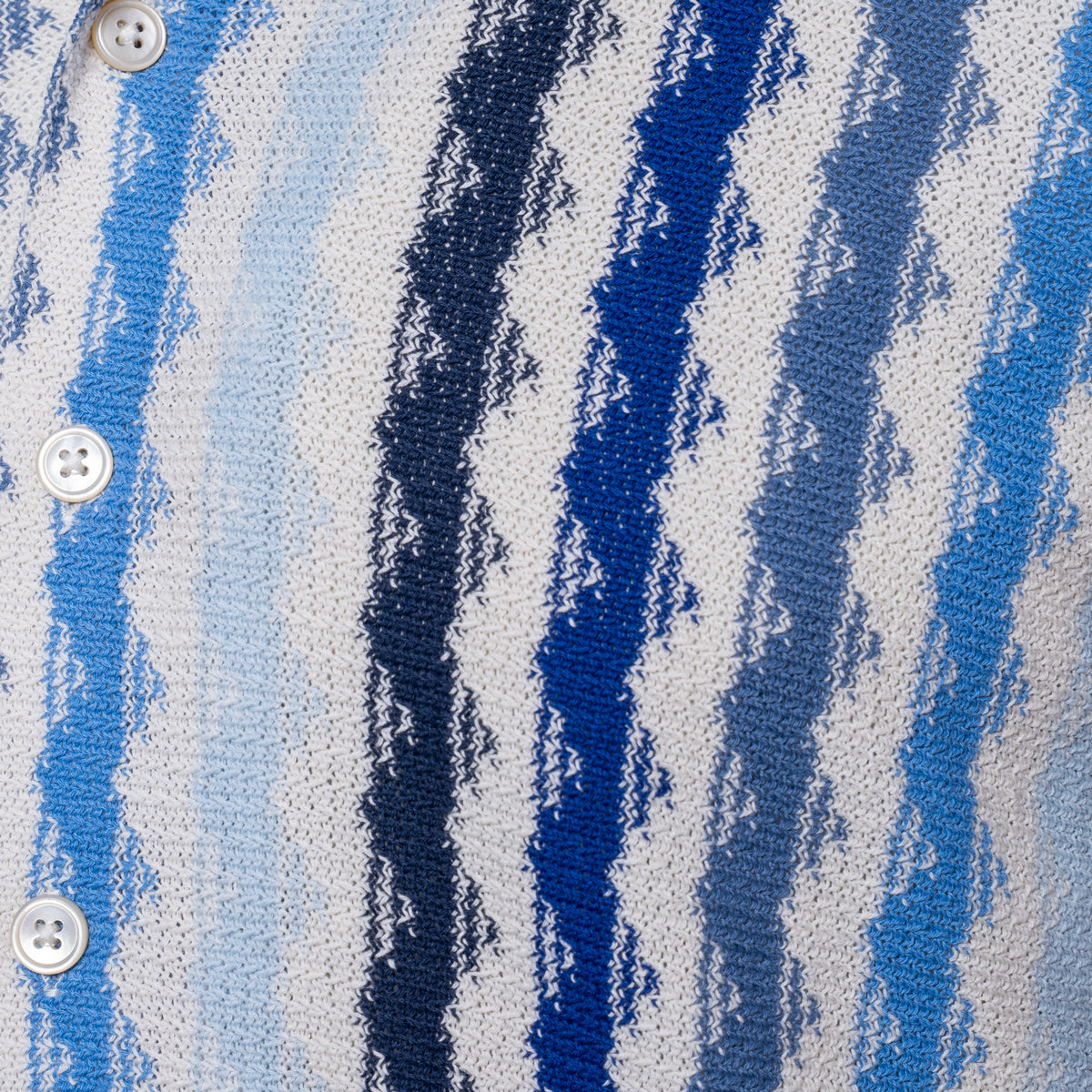 Close-up of a knit button-front garment with vertical wavy stripes in white, light blue, medium blue, and dark navy, showing white buttons along the left side. Gran Sasso Short Sleeve Shirt available at Sakks Menswear in Southampton.