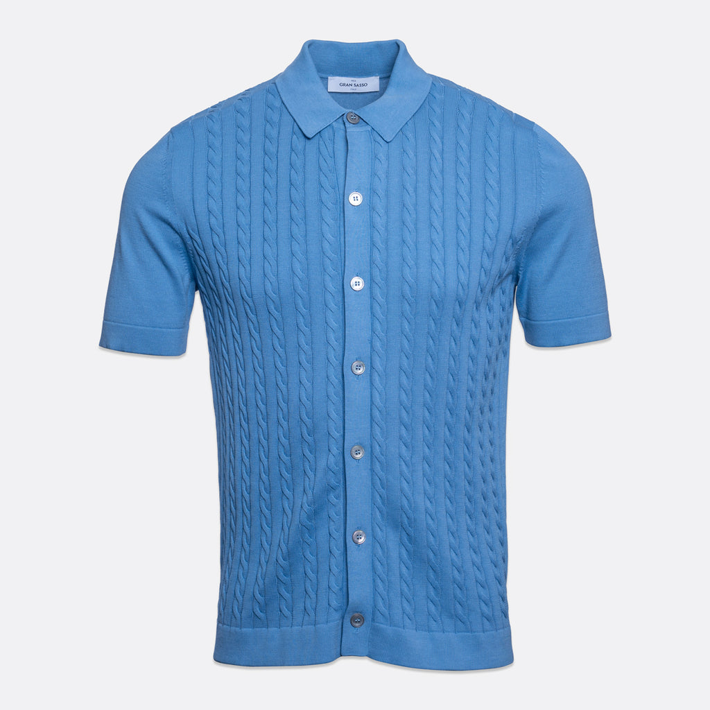 A light blue short-sleeve knit polo shirt with a cable-knit pattern on the front, a classic collar, and silver buttons, shown against a light grey background. Gran Sasso Polo available at Sakks Menswear in Southampton.
