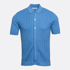 A light blue short-sleeve knit polo shirt with a cable-knit pattern on the front, a classic collar, and silver buttons, shown against a light grey background. Gran Sasso Polo available at Sakks Menswear in Southampton.