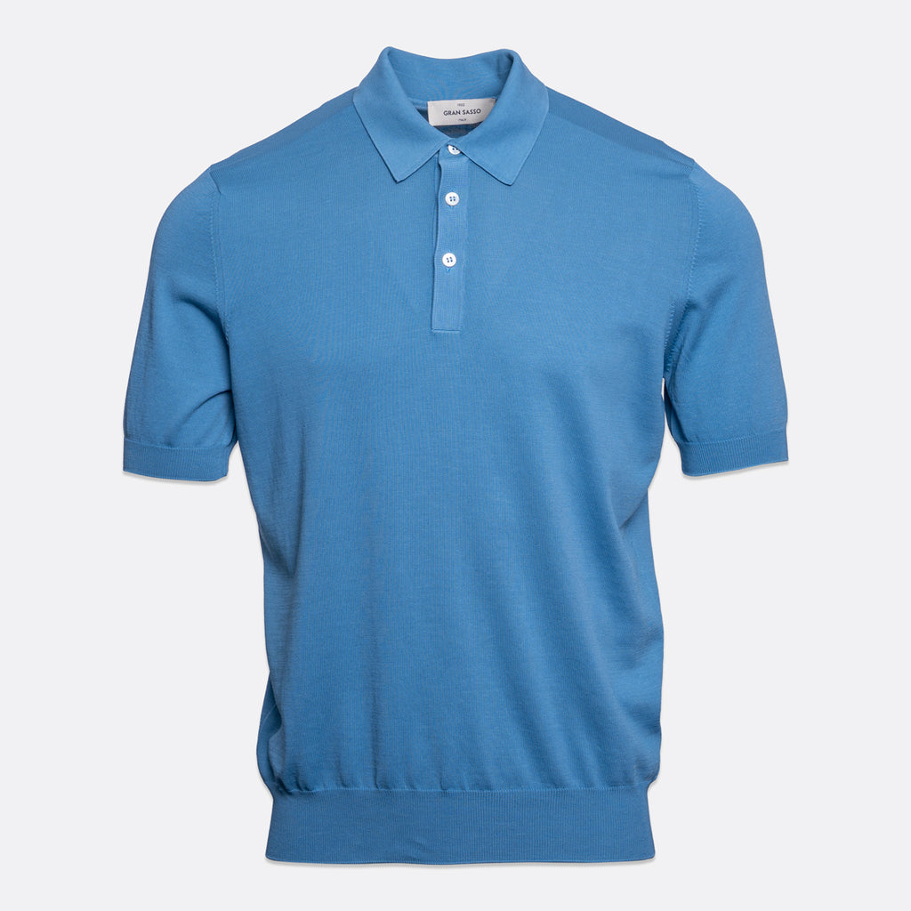 A short-sleeve polo shirt in a medium blue colour, featuring a classic collar, two-button placket, and ribbed cuffs and hem, shown against a light grey background. Gran Sasso Polo available at Sakks Menswear in Southampton.
