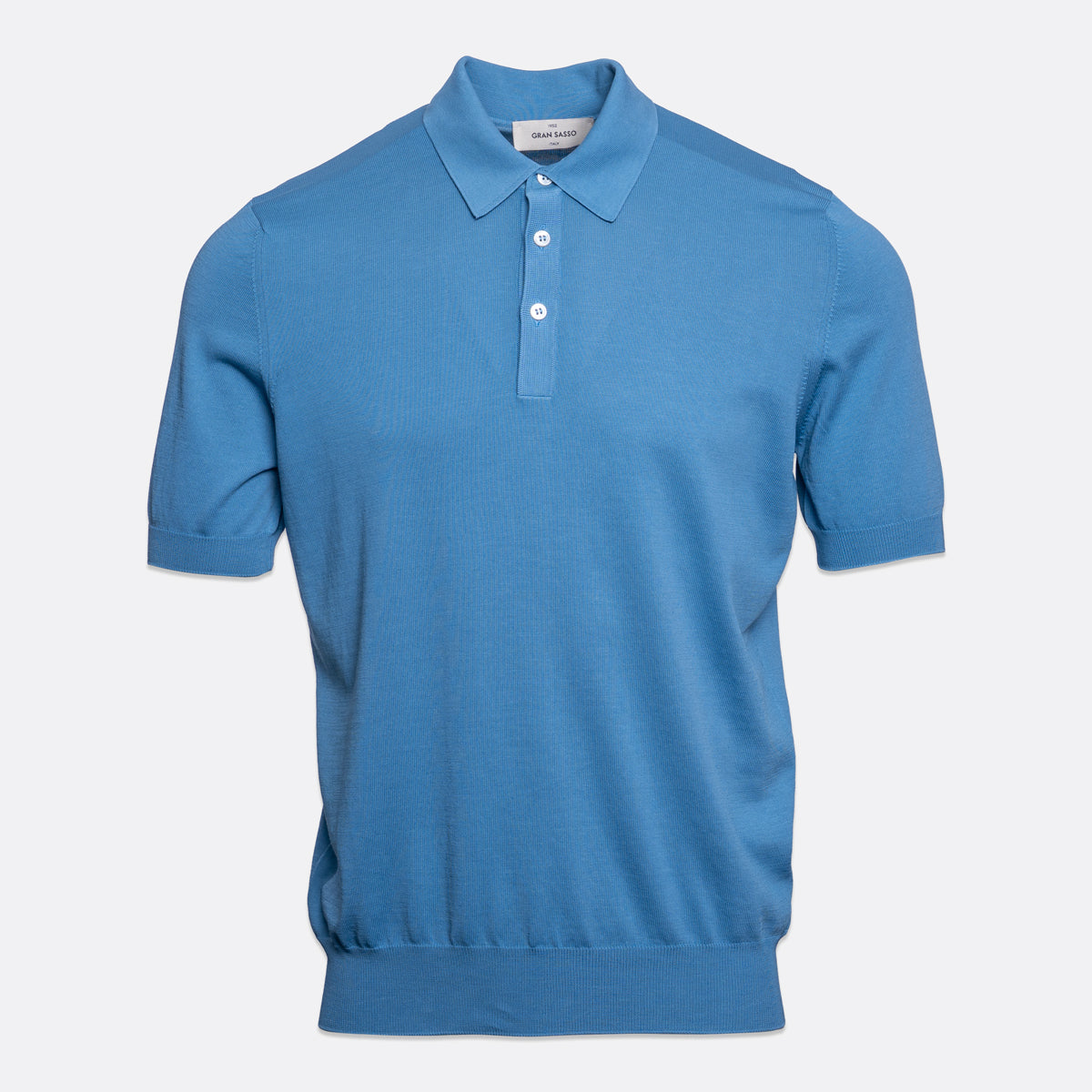 A short-sleeve polo shirt in a medium blue colour, featuring a classic collar, two-button placket, and ribbed cuffs and hem, shown against a light grey background. Gran Sasso Polo available at Sakks Menswear in Southampton.