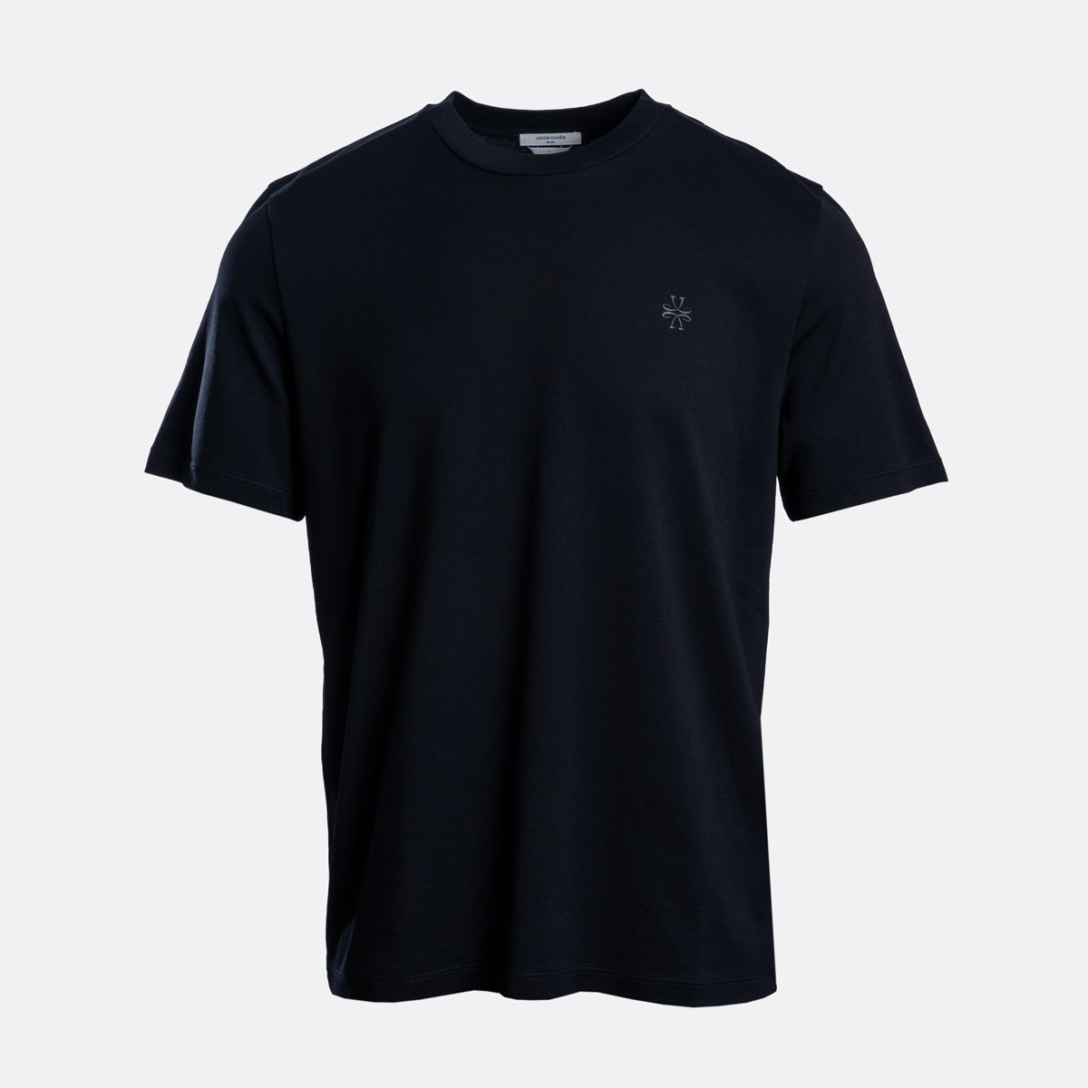 A dark navy blue short-sleeve crewneck t-shirt with a small embroidered cross logo on the left chest, displayed on a light gray background. Jacob Cohën T-Shirt available at Sakks Menswear in Southampton.