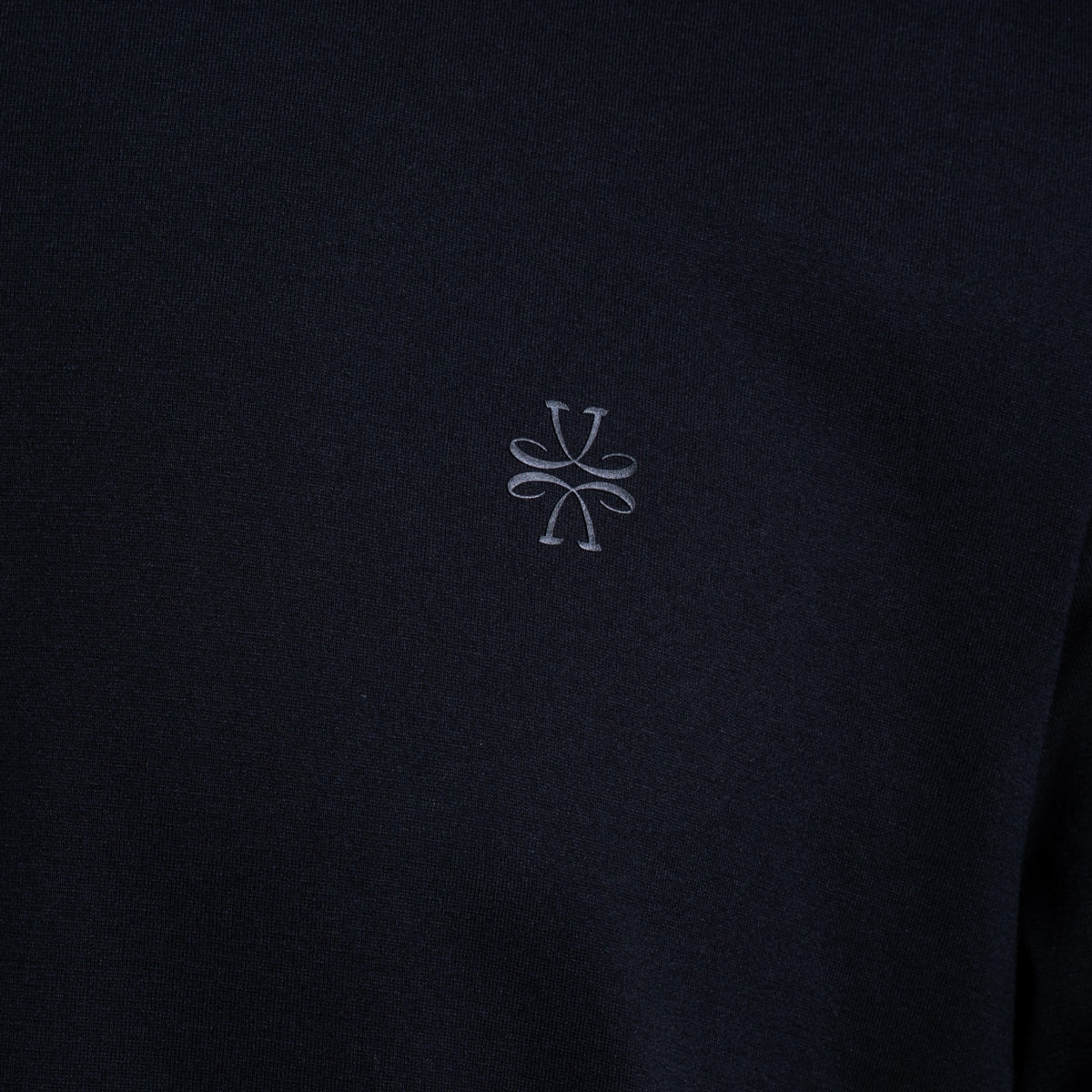 Close-up of a dark navy fabric with a small light gray embroidered logo in the center. Jacob Cohën T-Shirt available at Sakks Menswear in Southampton.