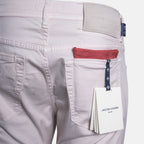 Close-up of the back waistband and right pocket of light pink denim jeans by Jacob Cohen, showing a red pocket lining, a dark blue brand tab, and a white hangtag. Jacob Cohën Chinos available at Sakks Menswear in Southampton.