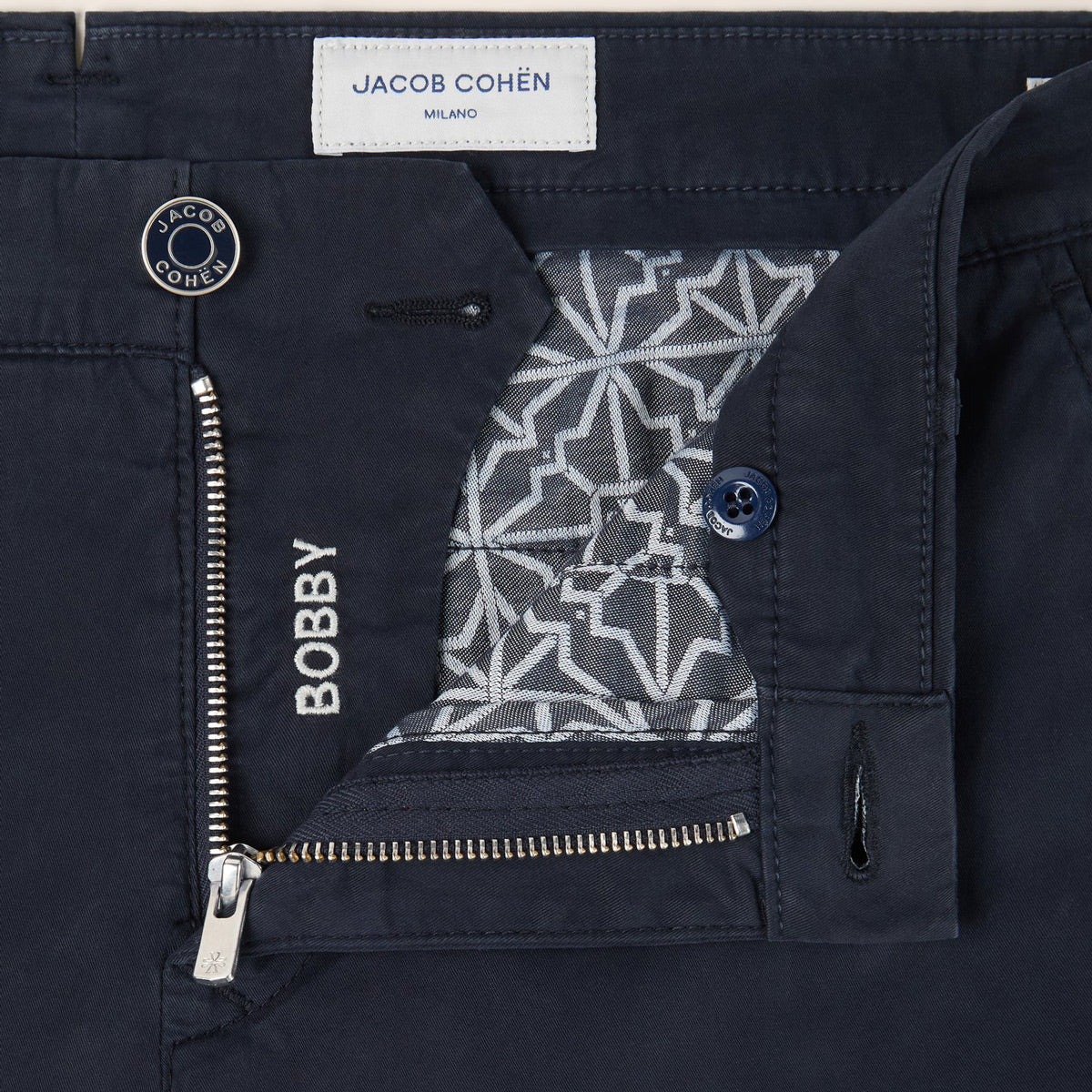 Close-up of dark navy blue jeans showing the inner pocket detail, a silver zipper with 'BOBBY' text, a patterned lining, and a visible JACOB COHÉN brand label. Jacob Cohën Chinos available at Sakks Menswear in Southampton.