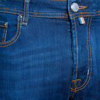 Close-up of a pair of blue denim jeans showing the waistband, button, pocket, and orange contrast stitching. Jacob Cohën Jeans available at Sakks Menswear in Southampton.