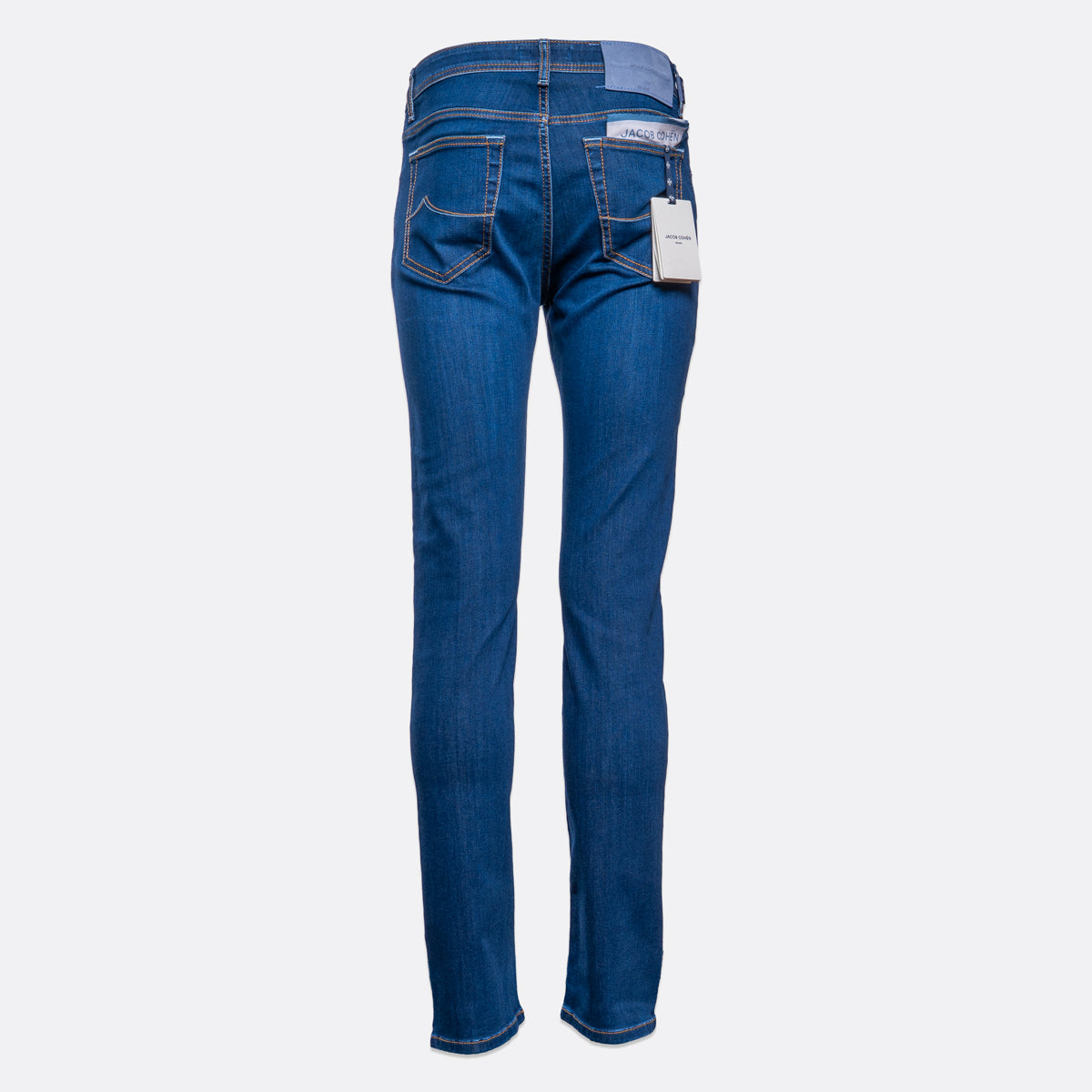 Back view of a pair of medium wash blue jeans with a white brand tag hanging from the back pocket, shown on a light gray background. Jacob Cohën Jeans available at Sakks Menswear in Southampton.