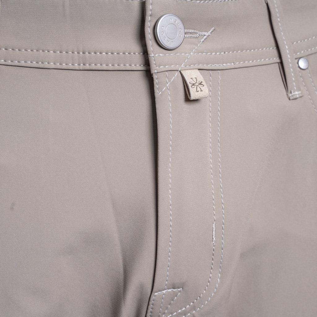 Close-up of the waistband of khaki trousers, showing a silver metal button, white contrast stitching, and a small beige fabric brand tag with a stylized logo. Jacob Cohën Chinos at Sakks Menswear in Southampton.