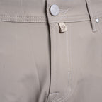 Close-up of the waistband of khaki trousers, showing a silver metal button, white contrast stitching, and a small beige fabric brand tag with a stylized logo. Jacob Cohën Chinos at Sakks Menswear in Southampton.