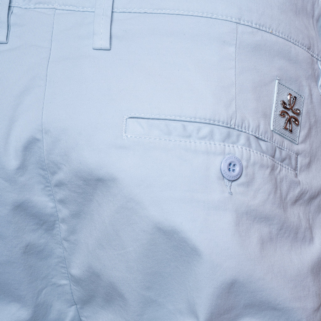 Close-up of the back waistband and pocket area of light blue shorts, showing a buttoned welt pocket, belt loops, and a small embroidered logo patch on the pocket. Jacob Cohën Shorts available at Sakks Menswear in Southampton.