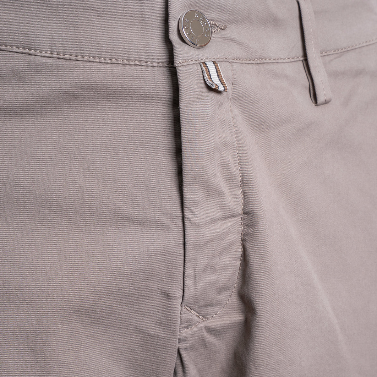 Close-up of a pair of light taupe-gray chino pants showing the waistband, button closure, belt loops, and front pocket stitching. Jacob Cohën Shorts available at Sakks Menswear in Southampton.