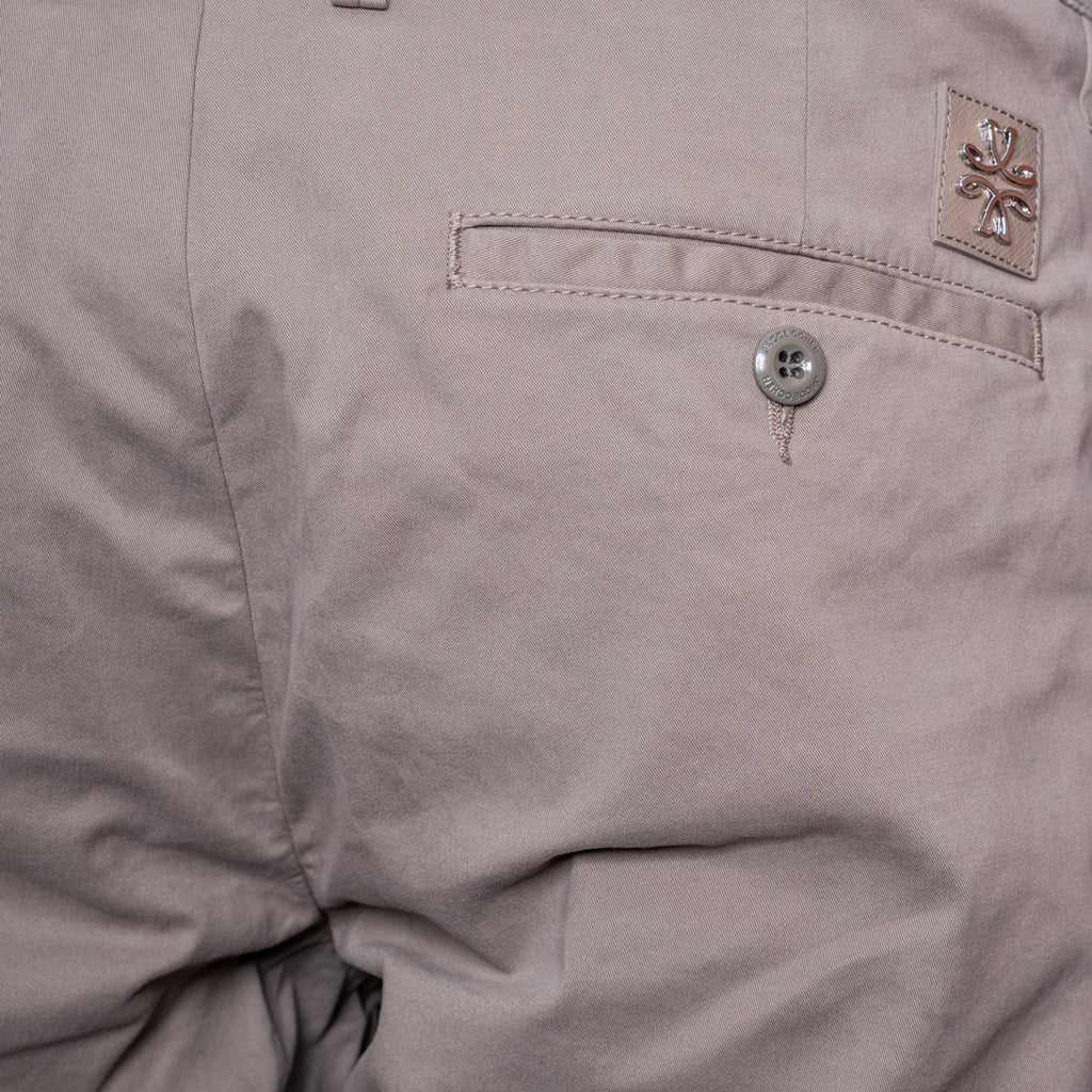 Close-up of a light taupe-gray pair of pants showing a pocket with a silver button and a small woven brand patch. Jacob Cohën Shorts available at Sakks Menswear in Southampton.