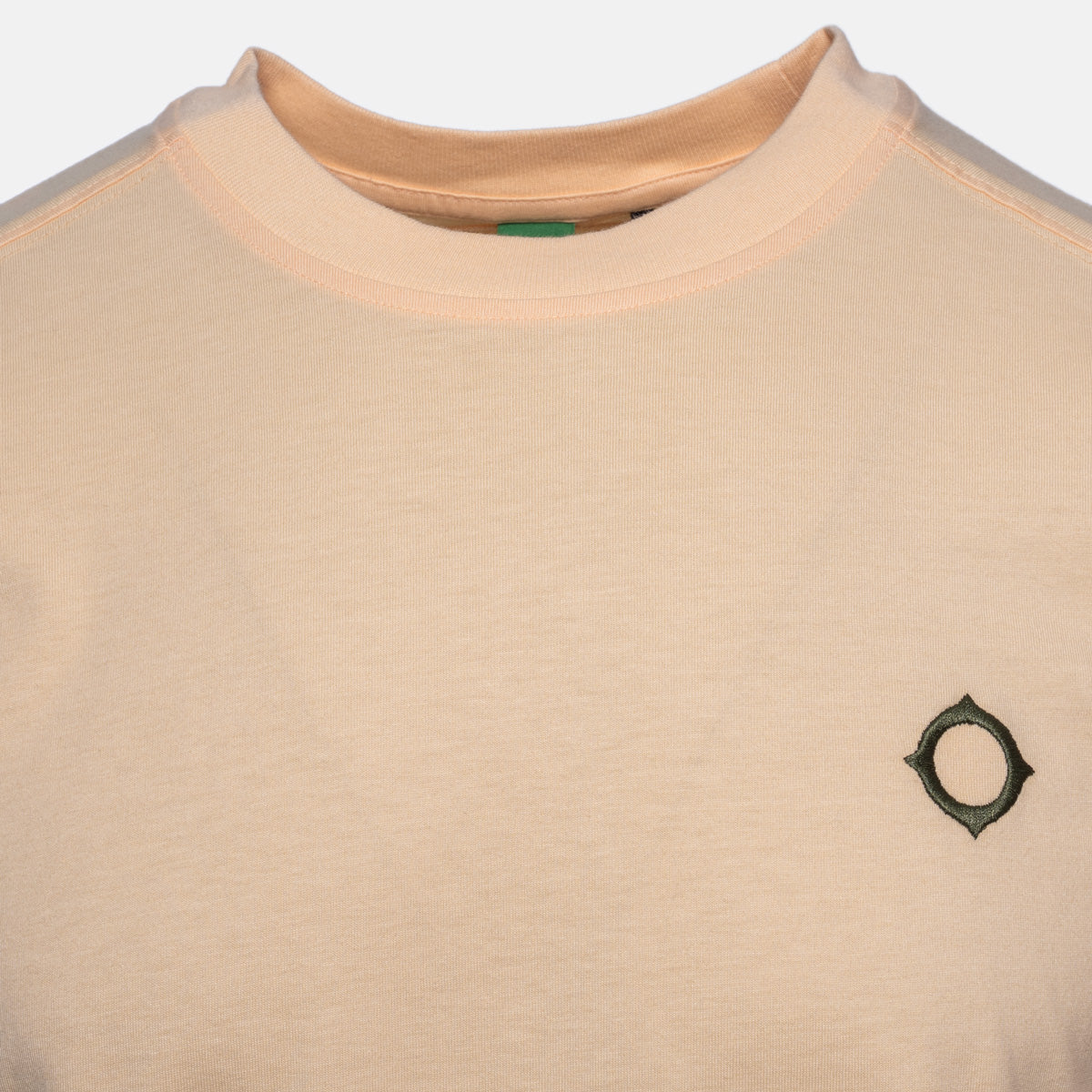 Close-up of a crewneck sweatshirt in a light peach-beige color, featuring a small dark green geometric logo on the left chest. MA.Strum T-Shirt available at Sakks Menswear in Southampton.