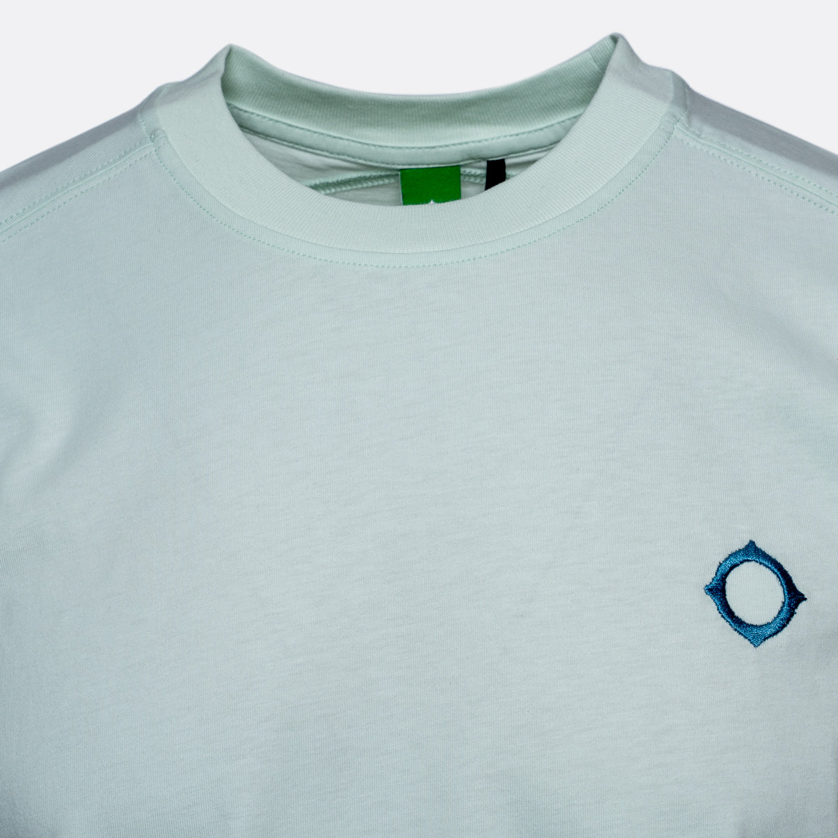 A close-up of a light mint green crewneck t-shirt featuring a small blue embroidered geometric logo on the left chest. MA.Strum T-Shirt available at Sakks Menswear in Southampton.